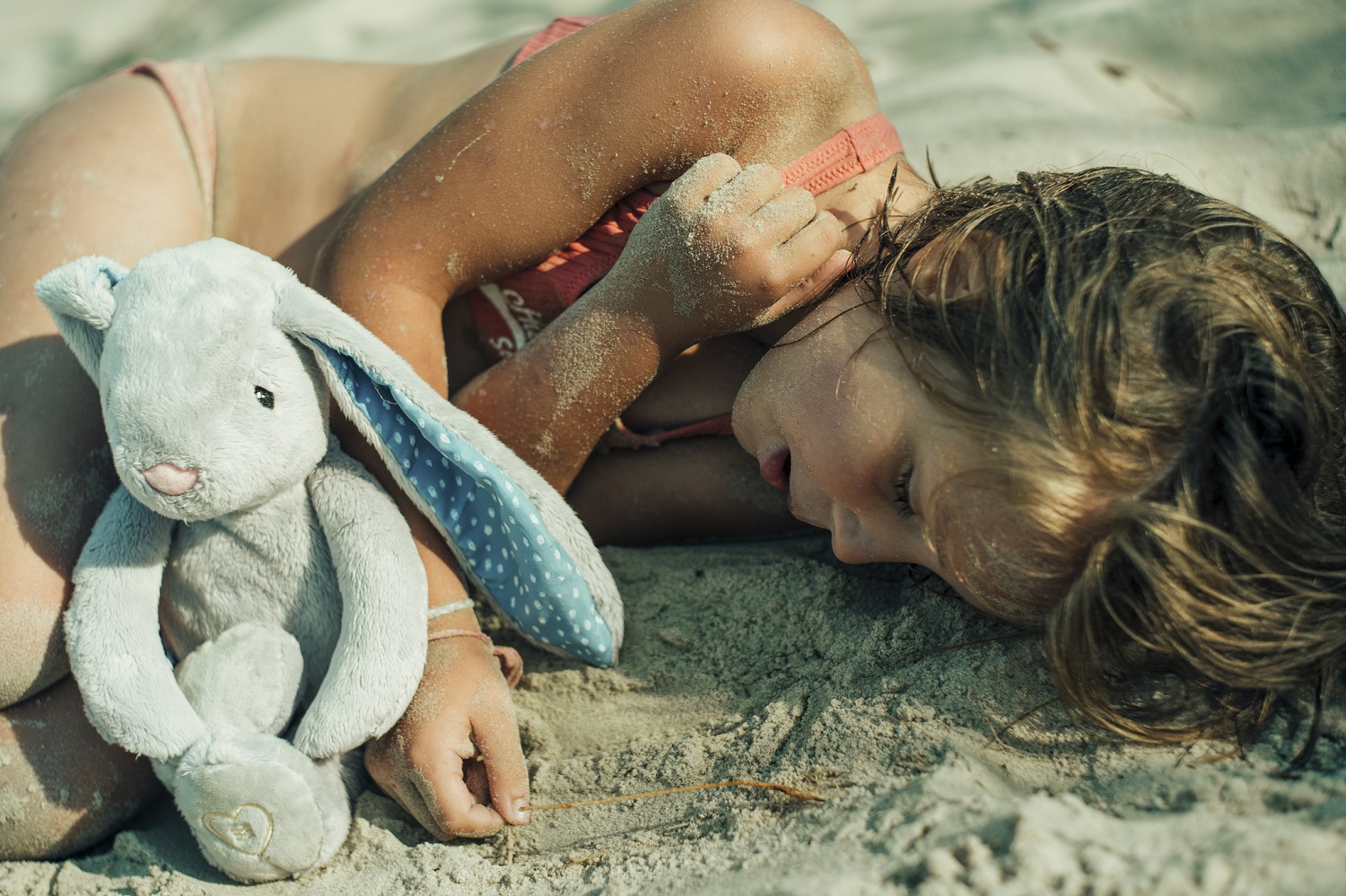 dziewczynka leży na plaży, obok niej szumiący króliczek Whisbear