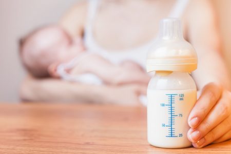 butelka mleka, w tle karmiąca dziecko matka